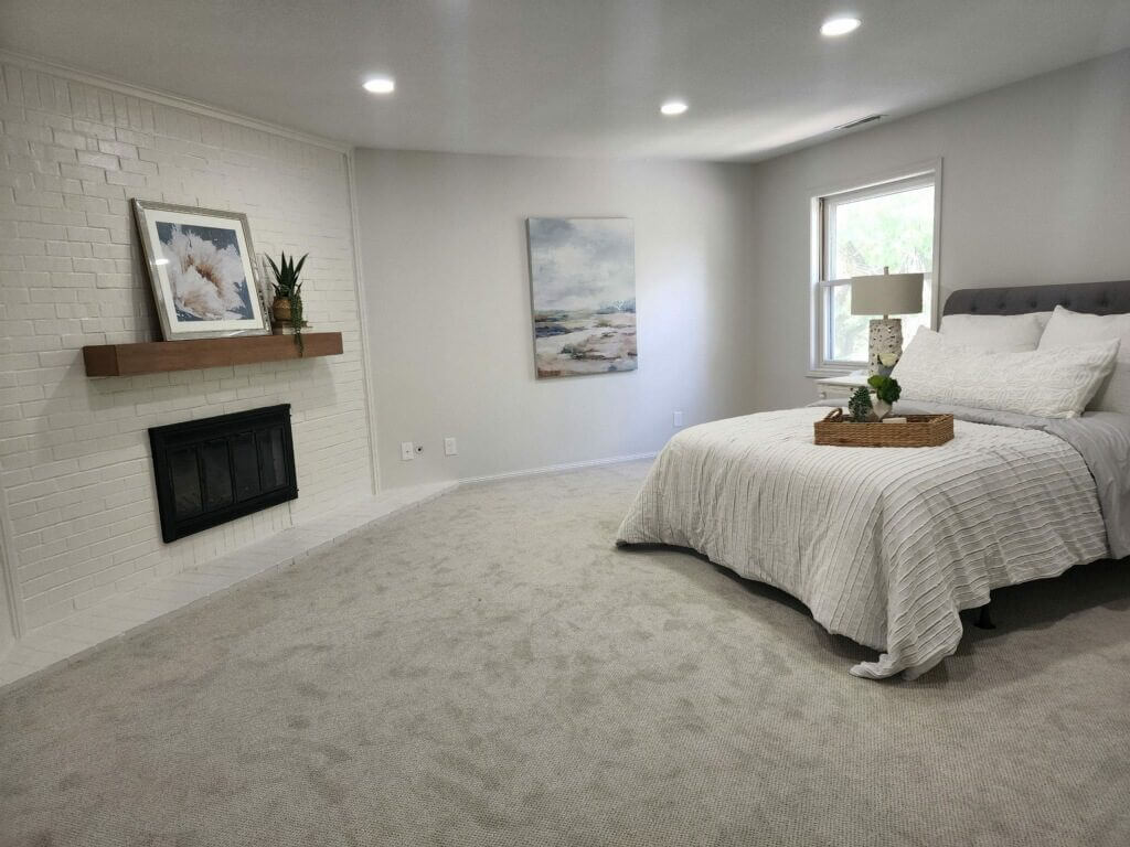 Modern master bedroom with queen size bed, brick fireplace, and neutral-colored wall, creating a cozy and stylish retreat