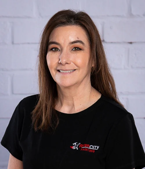 Office Coordinator, Leah Alvarez poses for an updated work headshot in 2025. She is wearing a black River City Painting embroidered scoop neck shirt and has straight shoulder length brown hair. Leah is in her late 40's with brown eyes and a great smile.